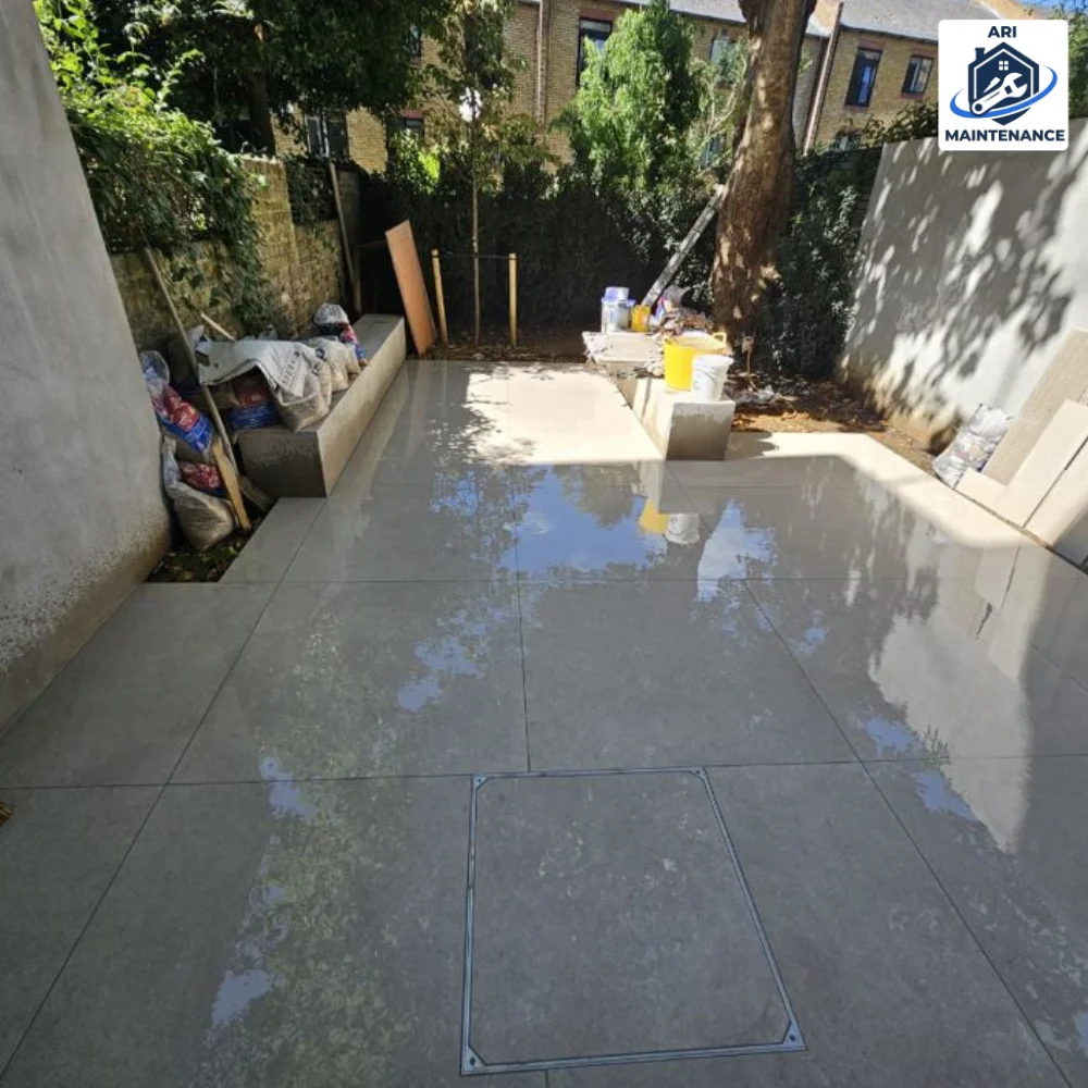 General repairs: rear garden patio laid in large-format grey concrete paving with a recessed inspection-cover tray, rendered boundary walls and raised planters