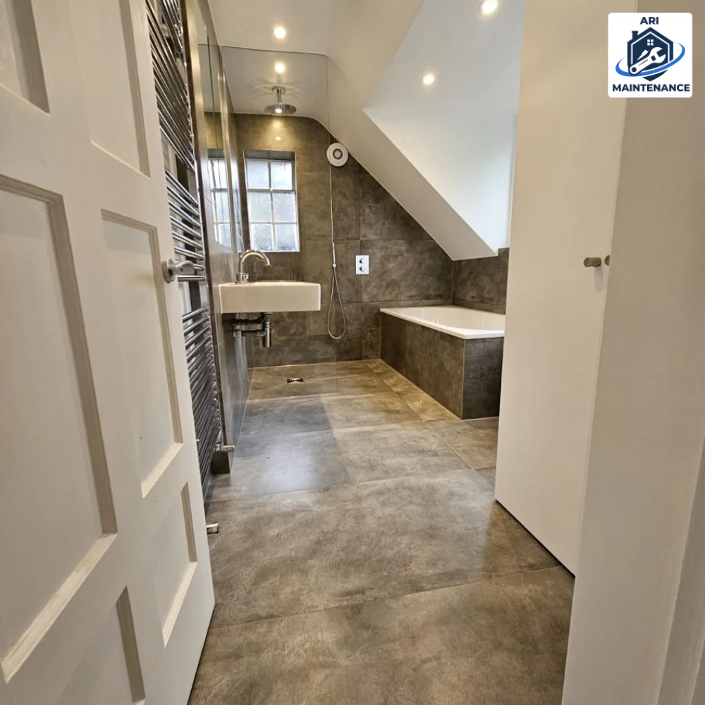 Bathroom refurbishment: loft bathroom with walk-in shower, polished-concrete-effect large-format tiling, tiled bath panel, wall-hung basin and chrome heated towel rail